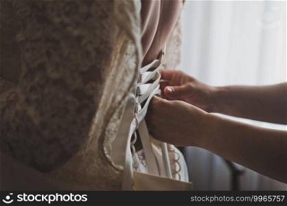 Womens hands lace up the brides wedding dress with a satin ribbon.. The brides wedding dress is laced with a satin ribbon 2597.