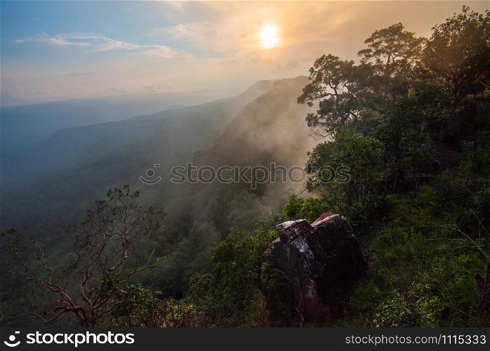 Wonderful landscape sunrise mountain with fog mist yellow and blue sky rising sunshine in the morning on hill top view jungle with rock on cliff tropical forest