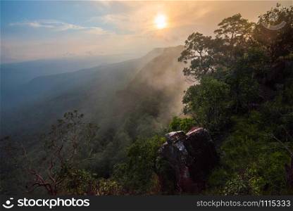Wonderful landscape sunrise mountain with fog mist yellow and blue sky rising sunshine in the morning on hill top view jungle with rock on cliff tropical forest