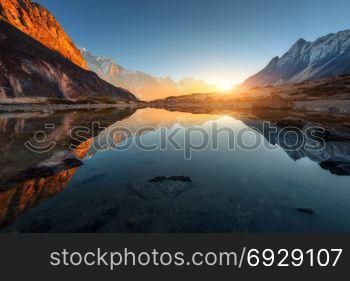 Wonderful landscape with high rocks with illuminated peaks, stones in mountain lake, reflection, blue sky and yellow sunlight in sunrise. Nepal. Amazing scene with Himalayan mountains. Himalayas