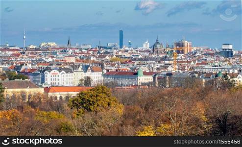 Wonderful urban landscape with roofs of historic and modern buildings in Vienna, Austria with autumn trees without leaves on a forefront on a blue cloudy background.. Urban landscape with roofs of historic and modern buildings in Vienna.