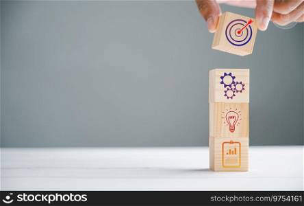 Wood block cube held by hand, featuring an icon that represents company strategy development. Conceptual image of achieving success and business goals.