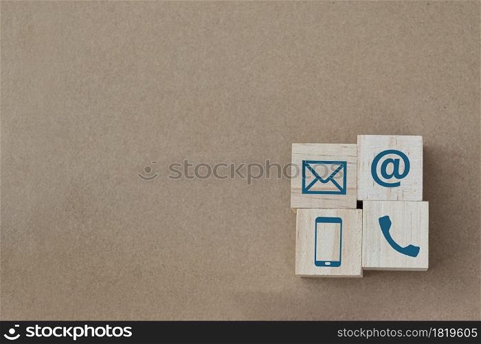 Wood cube with Phone, Email and Post Icons on brown paper background. copy space. Contact us.