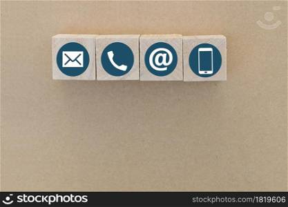 Wood cube with Phone, Email and Post Icons on brown paper background. copy space. Contact us.