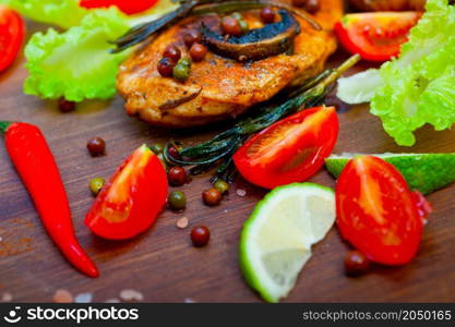 wood fired hoven cooked chicken breast on wood board with herbs spices and vegetables