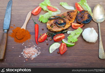 wood fired hoven cooked chicken breast on wood board with herbs spices and vegetables