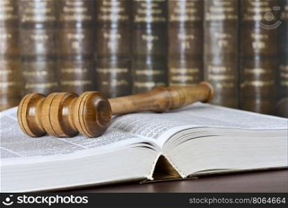 Wood gavel and open book on the background of shelves of old books