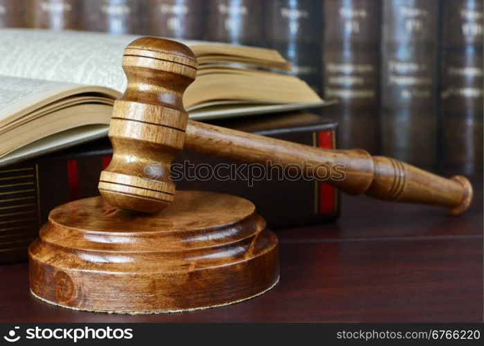 Wood gavel, soundblock and open book on the background of shelves of old books