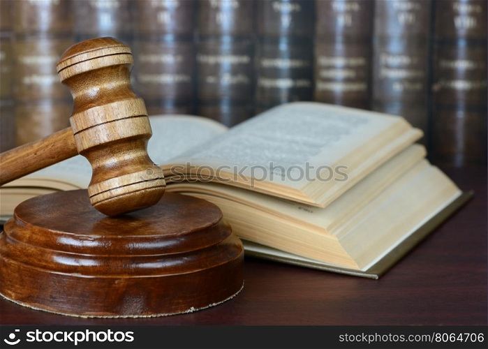 Wood gavel, soundblock and open book on the background of shelves of old books