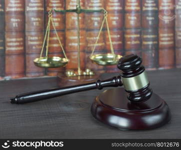 Wood gavel, soundblock and scales against the background of a row of antique books bound in leather