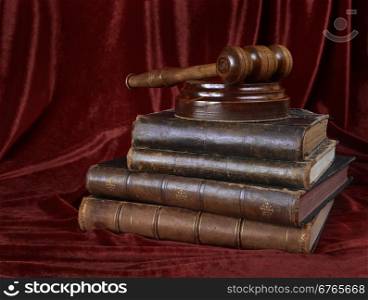 Wood gavel, soundblock and stack of thick old books against the background of red velvet