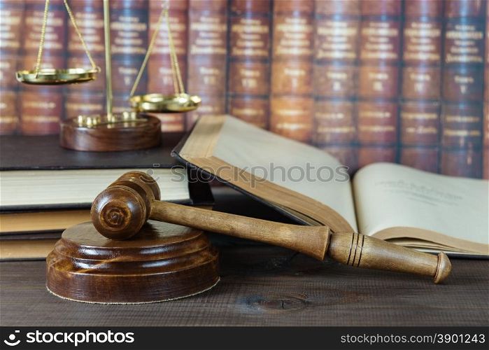 Wood gavel, soundblock, scales and open old book against the background of a row of antique books bound in leather