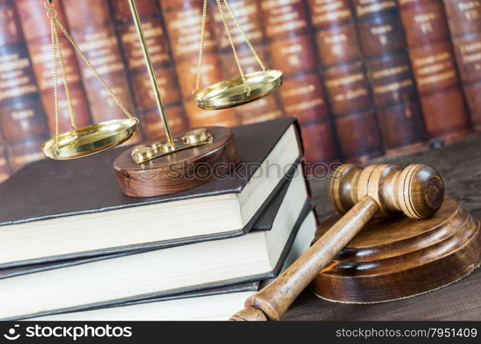 Wood gavel, soundblock, scales and stack of old books against the background of a row of antique books bound in leather