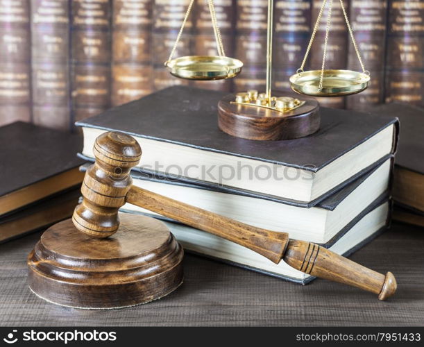 Wood gavel, soundblock, scales and stack of old books against the background of a row of antique books bound in leather