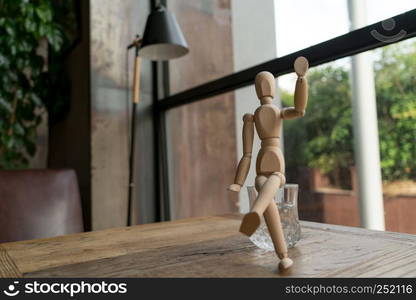 wood man is sitting on a glass of water while raise hand up