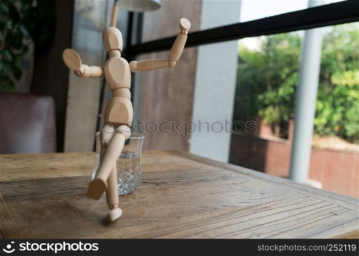 wood man is sitting on a glass of water while raise hand up