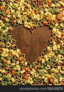 Wood table filled with heart-shaped pasta making a heart shape in the middle. 