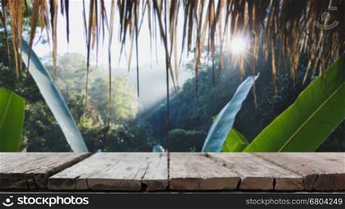 wood table for display your product and blur image of green tree in forest looking from inside the hut with sun rays for background usage
