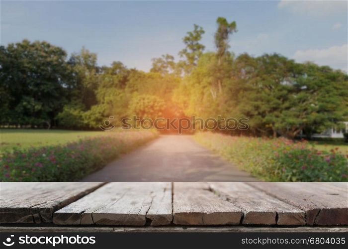 wood table for display your product with background of scenic road in park with beautiful flower along side
