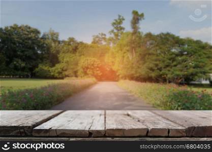 wood table for display your product with background of scenic road in park with beautiful flower along side