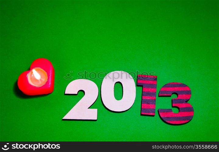 Wooden 2013 year number with a burning candle over green background