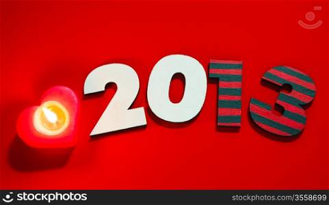 Wooden 2013 year number with a burning candle over red background