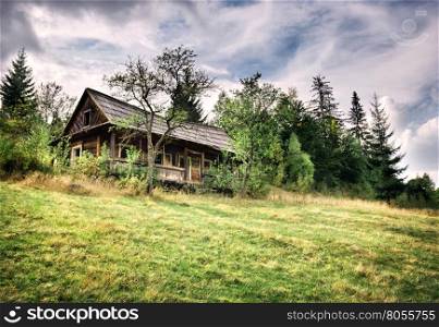 Wooden abandoned house among green trees under dramatic sky. Wooden abandoned house among green trees