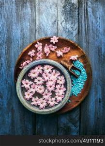 Wooden and blue bowl with pink flowers and water, scoop with sea salt on old background , top view