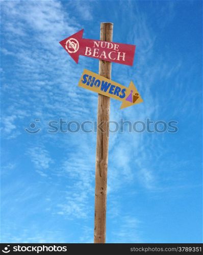 wooden arrow direction signs post to the nude beach and showers against a blue sky