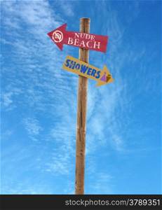 wooden arrow direction signs post to the nude beach and showers against a blue sky