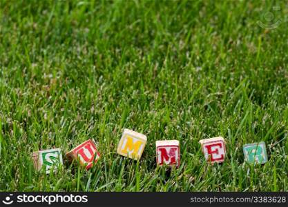 Wooden baby block spelling the word summer in grass