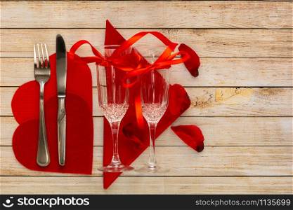 Wooden background with glasses of champagne, petals, hearts and cutlery. The concept of Valentine Day and restaurant romantic dinner. Top view with space for your greetings.