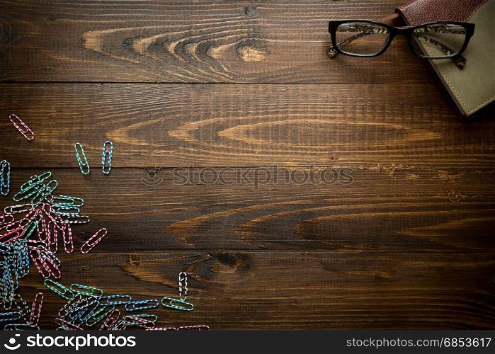 Wooden background with notebook and colorful paperclips. Place for text