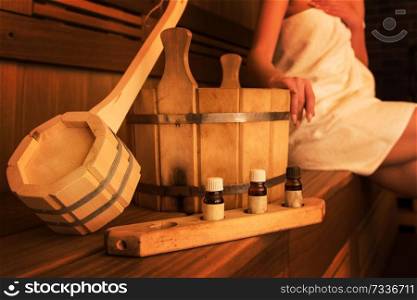 Wooden bath accessories with aromatic oil bottle for bath in the sauna and woman on background. Wooden bath accessories