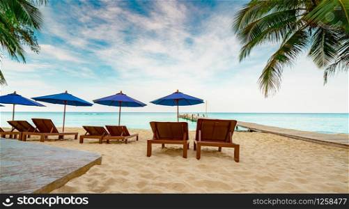 Wooden beach chair and beach umbrella at sand beach of resort beside the bridge. Summer vacation travel. Tropical holiday travel. Three couple sunbed and coconut tree with blue sky and white clouds.