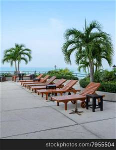 Wooden beach chairs at swimming pool with sea background
