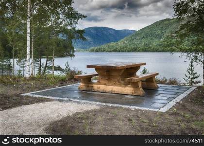 wooden bench at fjord in norway with the mountains and green forest as background