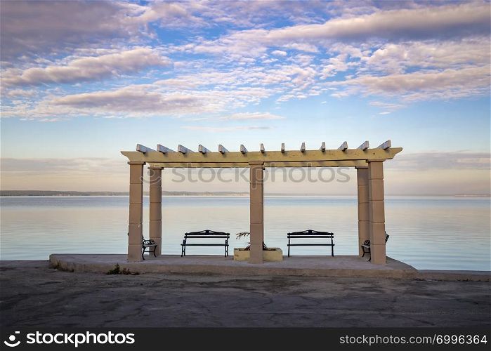 Wooden benches with a view at calm sea and colorful sky. Beautiful place for relaxing and enjoying nature. Traveling stop for travelers.