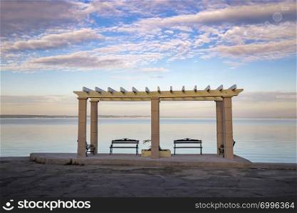 Wooden benches with a view at calm sea and colorful sky. Beautiful place for relaxing and enjoying nature. Traveling stop for travelers.