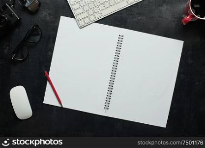 Wooden black office desk table with notebook, camera and other supplies with cup of coffee. Blank notebook page for input the text in the middle. Top view