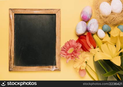 wooden blackboard with easter eggs fresh flowers yellow backdrop