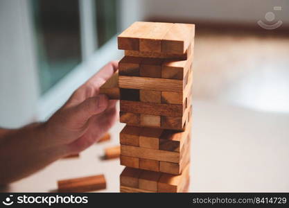 Wooden blocks toy puzzle with human hand on table at home background. Entertainment and business concept.