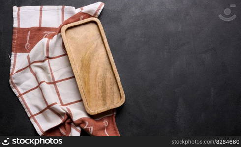 Wooden board and folded linen linen kitchen towel on a black background, top view. Copy space