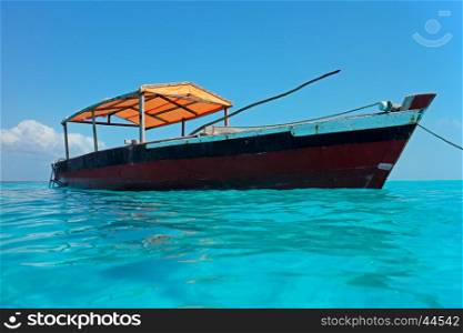 Wooden boat floating on the clear turquoise water of Zanzibar island