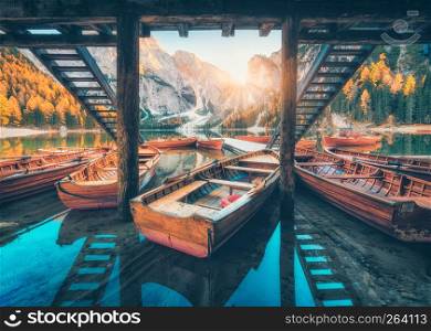 Wooden boats near the house in Braies lake at sunrise in autumn in Dolomites, Italy. Scenery with mountains, pier, boat, reflection in water, trees in fall. Travel in Europe. Dolomiti. Italian alps
