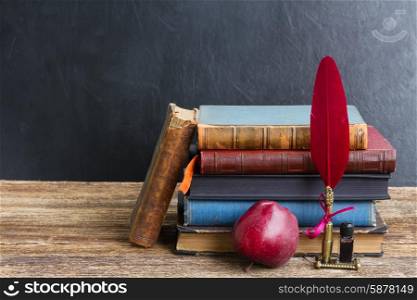 Wooden bookshelf with antique books, apple and red feather pen