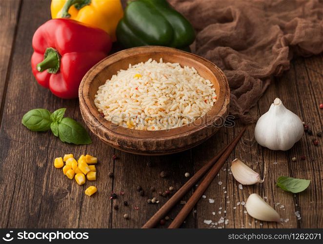 Wooden bowl with boiled long grain basmati rice with vegetables on wooden table background with sticks and paprika pepper with corn,garlic and basil.