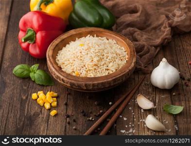 Wooden bowl with boiled long grain basmati rice with vegetables on wooden table background with sticks and paprika pepper with corn,garlic and basil.