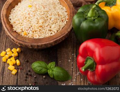 Wooden bowl with boiled long grain basmati rice with vegetables on wooden table background with paprika pepper with corn and basil.