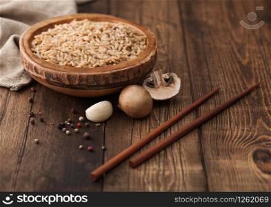 Wooden bowl with boiled long grain risotto rice with mushrooms on wooden background with sticks and linen kitchen towel.